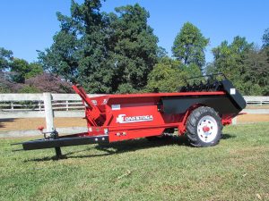 ground driven manure spreader sitting along white fence 1